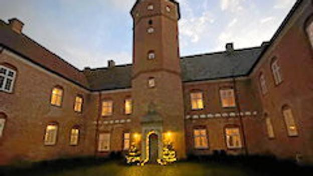 Nørlund Slot ved aftenstide med lys i juletræer omkring hovedindgangen. Privatfoto