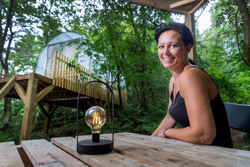 Ina Grønhøj ved et af skovteltene, der alle er placeret på et podiet af træ hævet et godt stykke over skovbunden.