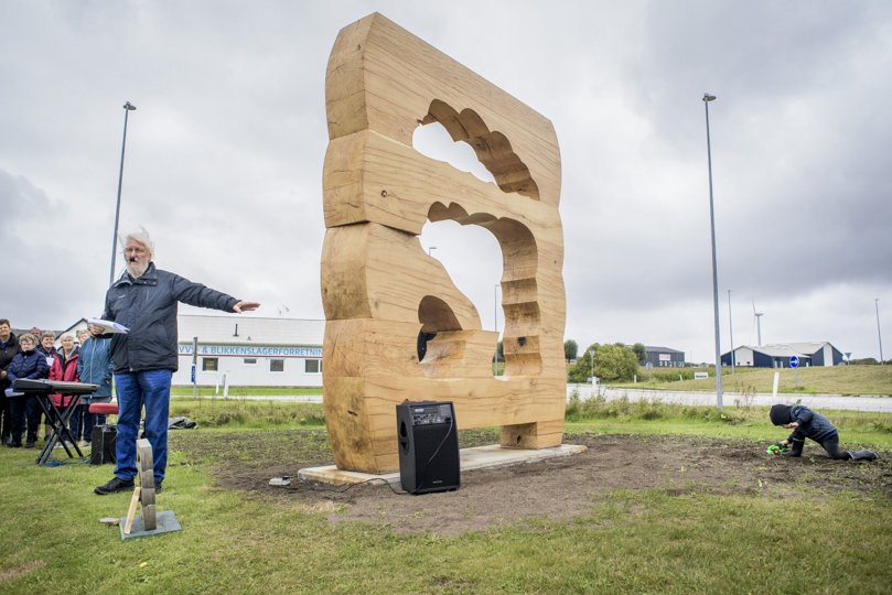 Erland Knudssøn Madsen fortæller om den godt tre meter høje skulptur i massivt egetræ - mens en af de yngste gæster til højtideligheden har travlt med at grave.