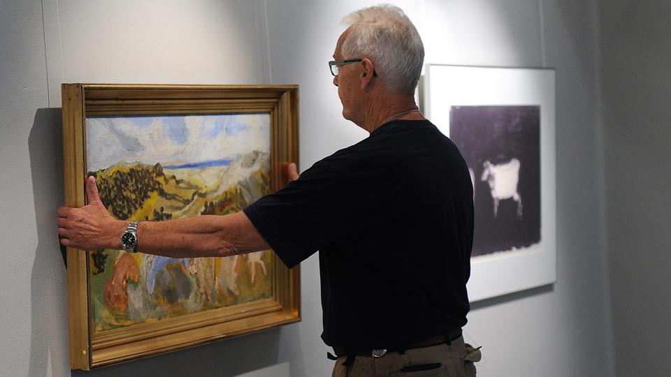 Fredag var ophængningen stadig i gang. Her er det museumsmedarbejder Ib Nielsen med et af Jens Søndergaards malerier - berømt for sin blå ko.
Foto: Diana Holm <i>diana.holm@nordjyske.dk</i>