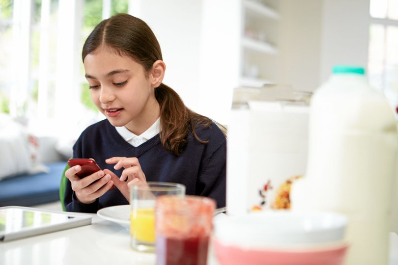Schoolgirl With Digital Tablet And Mobile At Breakfast