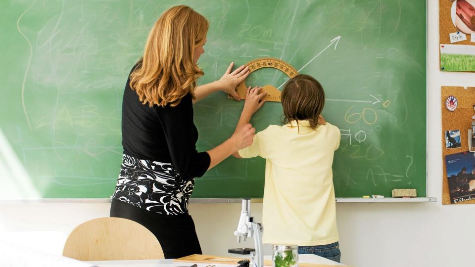 ©Michèle Constantini/AltoPress/Maxppp ; Teacher helping boy draw angle on blackboard using protractor, rear view <i>AltoPress / Maxppp</i>
