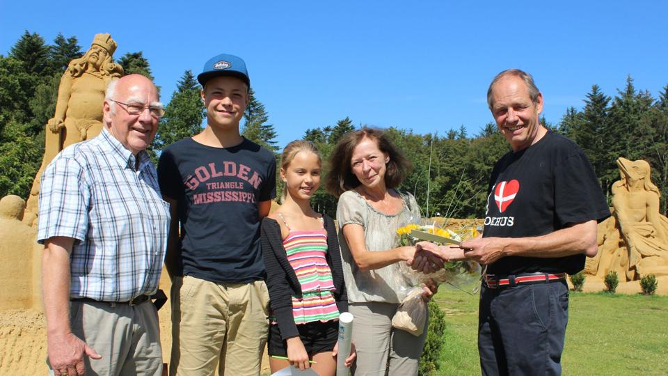 John Andersen, indehaver af Blokhus Sandskulptur Festival overrækker gaver til den heldige familie, som gæstede parken som nummer 50.000. foto: Lotte Kande