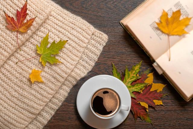 Cup of coffee, book, autumn leaves ans wool scarf on table