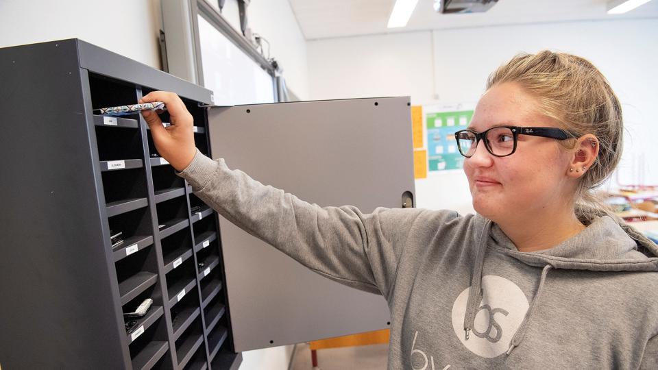 Iben Skovmose lægger sin mobiltelefon ind i skabet, der har en lille hylde med navne til hver af de 17 elever i 9.a på Hanstholm Skole. Og det samme gør de fleste i klassen, efter at der er blevet indført en ny regel om, at man kan få udleveret mobilen i det store frikvarter. Foto: Peter Mørk