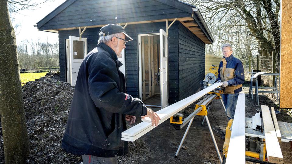 Pensioneret tømrersvend og tovholder for byggeprojektet i søanlægget i Haverselv Vagner Andreasen (bagerst) får hjælp af frivillig John Hansen til at save og montere de udvendige udhængsbrædder på fælleshuset.