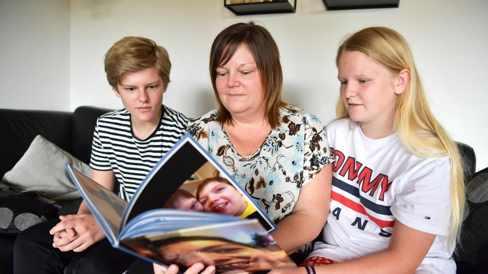 Patrick på 16 og Julie på 13 år kigger sammen med deres mor, Lotte Holm, i mindebogen om storebroderen Mathias, som døde for halvandet år siden. Foto: Claus Søndberg