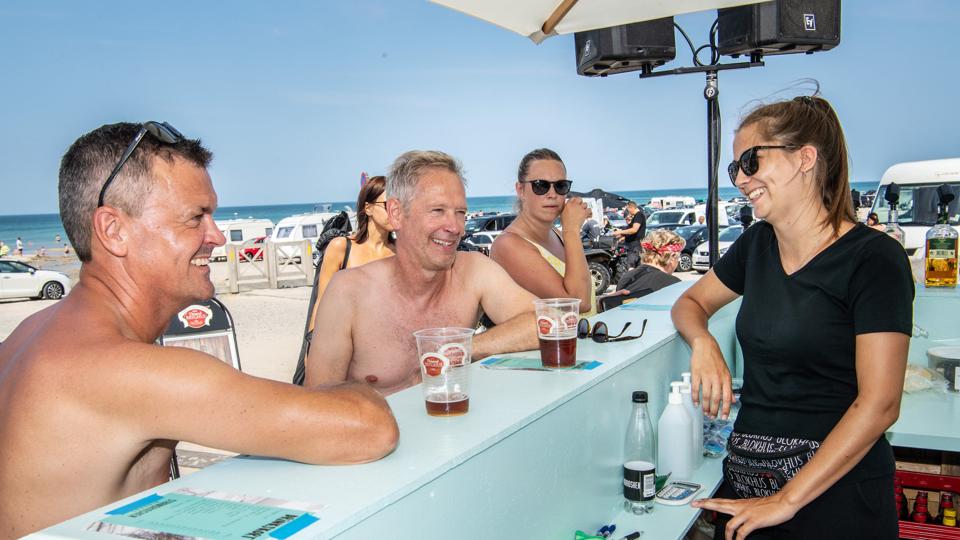 Brian Kornum (tv) og Ole Jensen (th) får sig en drink og en snak med bartenderen Jeanette Aakjær ved indløbet til stranden.