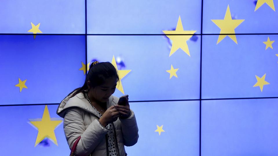 A visitor uses her mobile phone in front of an electronic board in the atrium of the European Council building in Brussels <i>François Lenoir/Reuters</i>
