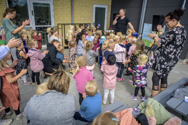 Børnene synger og danser udenfor, mens de voksne lytter til leder Heidi Lynggreens tale indenfor.
