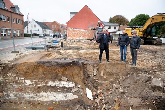 I Brønderslev midtby giver dette hul i jorden grund til smil hos Peter Stecher (K), formand for teknik- og miljøudvalget. De tre bygninger, der forsvinder i Vestergade markerer starten på omdannelsen af den nærliggende Banegårdspladsen. Fra venstre ses Peter Stecher, projektleder Kristian Hedver og leder af teknisk forvaltning, Benn Erik Grav. <i>Foto: Bente Poder</i>