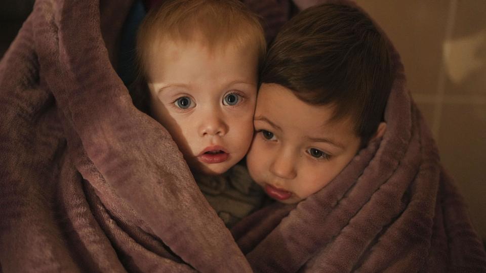 Et par ukrainske børn varme sig selv under et tæppe i havnebyen Mariupol, der i mange dage har været under belejring af russiske soldater. <i>Evgeniy Maloletka/Ritzau Scanpix</i>