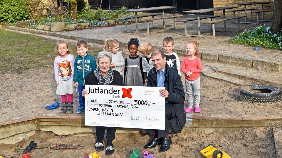 Arrangørerne bag Børnenes Grundlovsdag 2015 i Vesthimmerland er på sponsorjagt. Her afleverer afdelingsdirektør Brian Mikkelsen fra Jutlander Bank i Aars et tilskud på 3.000 kroner til Bodil Mikkelsen fra Børnehaven Lillevangen i Aars. Privatfoto