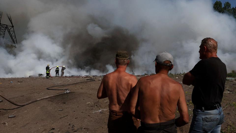 En gruppe mænd ser på, mens ukrainske brandfolk forsøger at slukke ilden efter endnu et russisk angreb i Kharkiv-regionen. Fotoet er taget mandag. <i>Leah Millis/Reuters</i>
