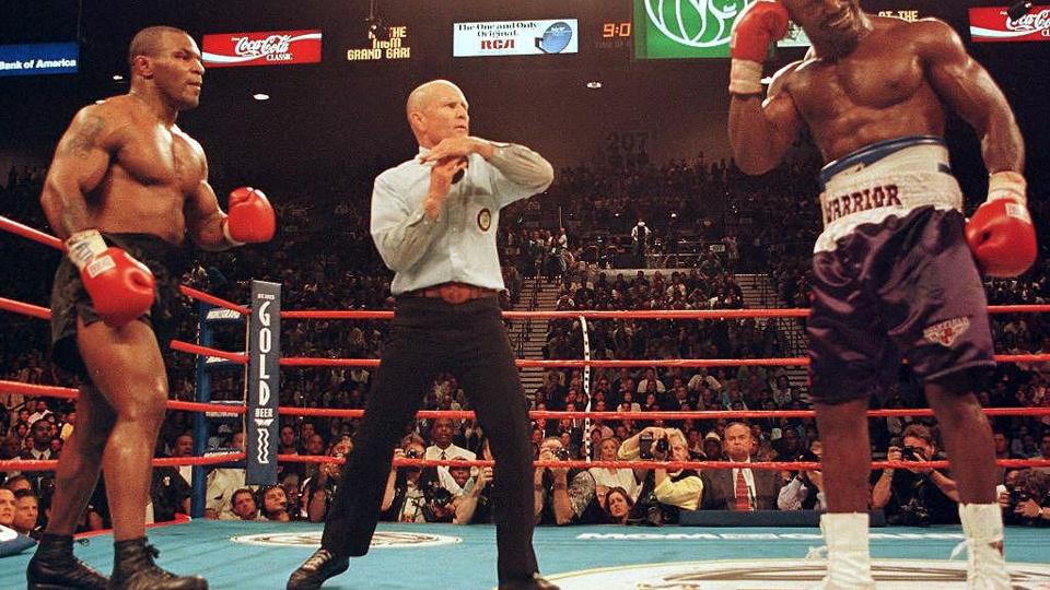 Kamplederen Lane Mills blev nødt til at stille sig ind i midten af ringen og stoppe boksekampen mellem Mike Tyson (til venstre) og Evander Holyfield. Holyfield tog sig til øret, fordi Tyson lige havde bidt en luns af det. Tyson blev kort efter diskvalificeret. Kampen blev bokset i MGM Grand Garden Arena i Las Vegas 28. juni 1997. <i>Epa/Ritzau Scanpix</i>