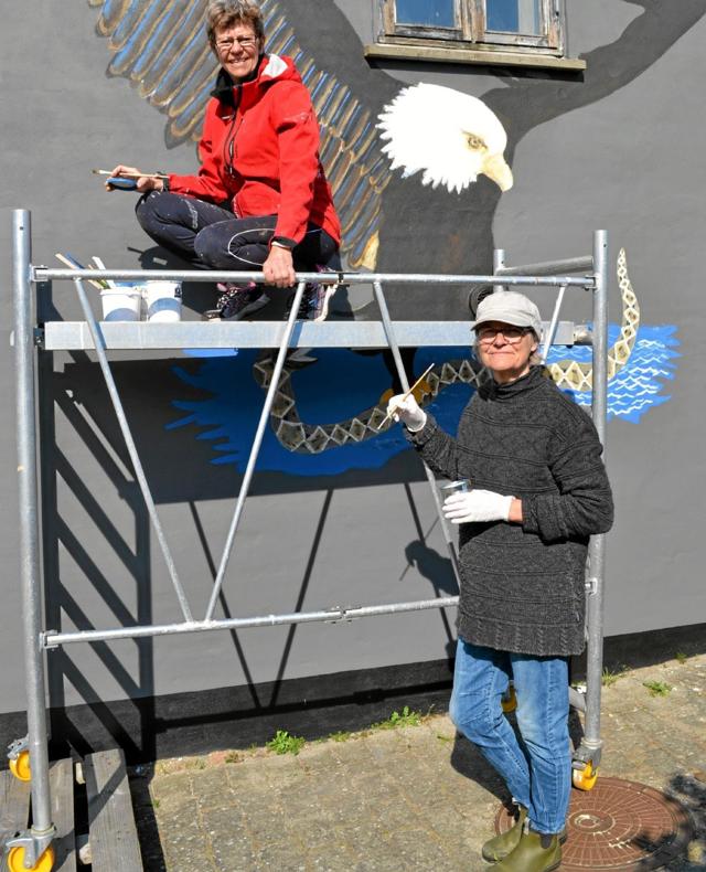 To medlemmer af Byforskønnelsesgruppen, Martha Christensen (i rød jakke) og Susanne Nielsen, er ”tyvstartet” med at opmale gavlmaleriet af ørnen på gavlen af et hus i Havnegade. ?Foto: Ole Torp
