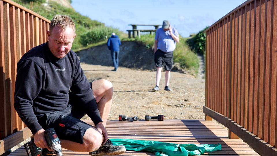 Ronny Hansen fra Wood-ways.com monterer de sidste broplanker. Broen har kostet 163.000 kroner plus moms ud af en samlet investering på godt to millioner kr.