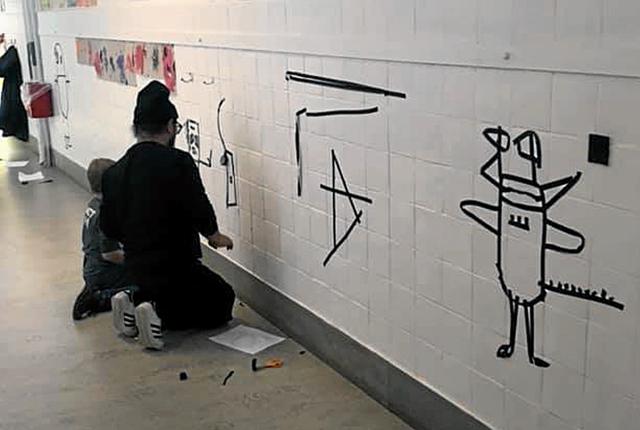 Kunstneren Phuc Van Dang er sammen med en elev ved at flytte et monster, der er tegnet på papir, til væggen som et skyggebillede med sort tape. Privatfoto
