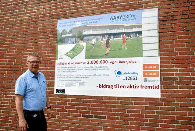 Henrik Pedersen foran Aabybro IF’s nuværende klubhus, hvor et banner fortæller om projektet med at få et nyt foreningshus. ?Foto: Bitten Holmsgaard