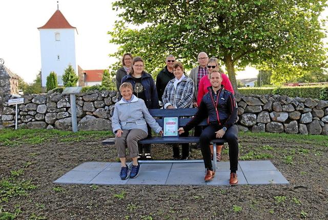 De seks bænke er alle placeret på strategisk velvalgte steder rundt omkring i Døstrup. Her har de involverede taget opstilling omkring bænken, der er opstillet ved Døstrup Kirke. Foto: Erik Røgild
