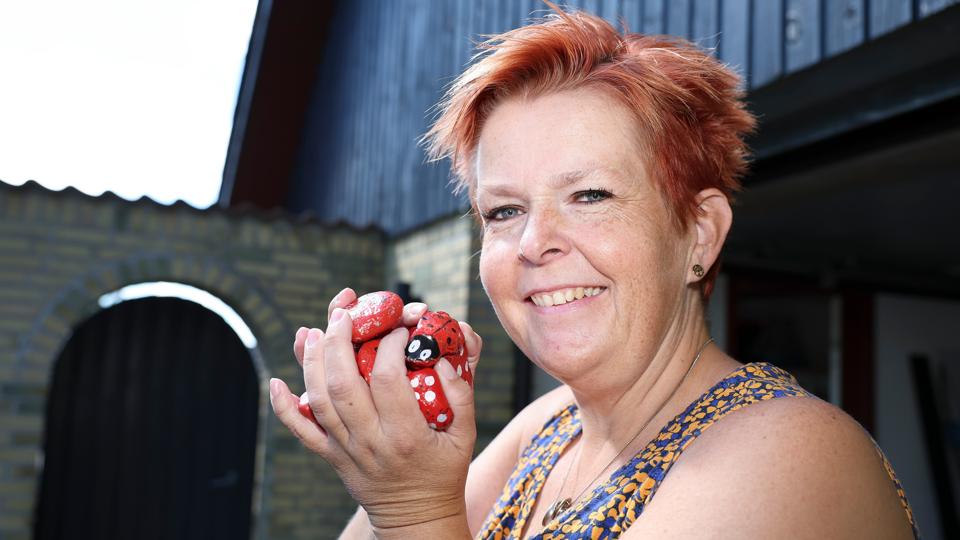 Britta Langkilde har gennem flere år lavet en sjov sommeraktivitet for børnene i Tårs. Hun gemmer malede sten rundt omkring i byen - og når byens børn så finder stenene, kan de møde op hos Britta og hendes mand og indkassere en isvaffel. Den lille leg er blevet vældigt populær i byen, og den giver parret masser af gode oplevelser og masser af smil til initiativtagerne. De røde sten, som Britta Langkilde holder her, blev brugt i "stenlegen" sidste år. I år er det grønne sten, hun har gemt i byen. <i>Foto: Bente Poder</i>