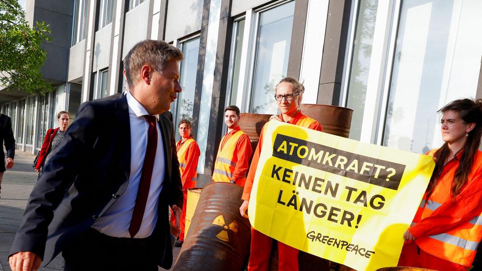 På vej til et pressemøde mandag går den tyske økonomiminister, Robert Habeck, forbi en Greenpeace-aktivist, der holder et skilt med teksten "atomkraft? Ikke en dag længere!" På pressemødet har den tyske regering meddelt, at den planlægger at forlænge levetiden for to atomkraftværker, så der er el til vinteren. <i>Michele Tantussi/Reuters</i>