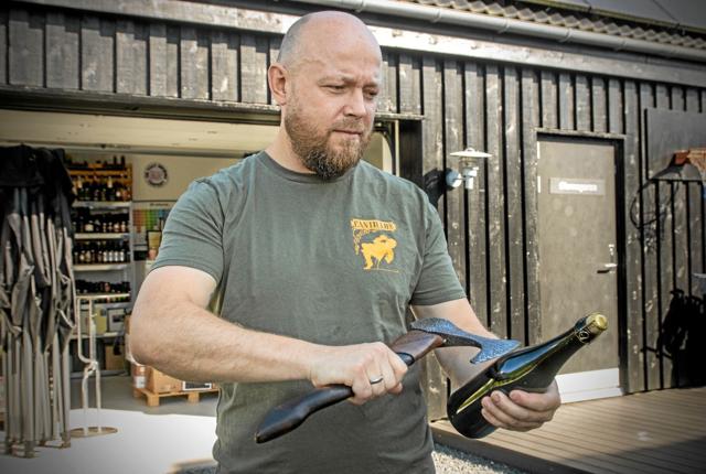 Jesper Mørkholt viser, hvordan man slår proppen af en ølflaske med en økse, når han lørdag står i spidsen for en beerwalk på Gjøl. Foto: Jesper Hansen