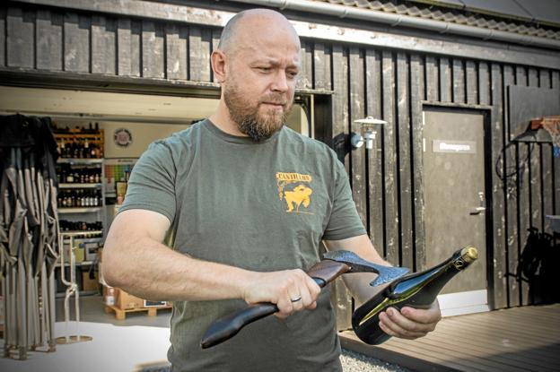 Jesper Mørkholt viser, hvordan man slår proppen af en ølflaske med en økse, når han lørdag står i spidsen for en beerwalk på Gjøl. Foto: Jesper Hansen