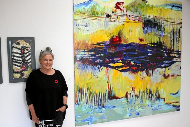 Lene Frederiksen ved sit største maleri, hvor hun for tiden har fokus på fantasiens landskab. Foto: Tommy Thomsen