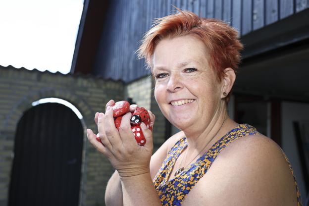 Britta Langkilde har gennem flere år lavet en sjov sommeraktivitet for børnene i Tårs. Hun gemmer malede sten rundt omkring i byen - og når byens børn så finder stenene kan de møde op hos Britta og hendes mand og indkassere en isvaffel. Den lille leg er blevet vældigt populær i byen, og den giver parret masser af gode oplevelser og masser af smil til initiativtagerne. De røde sten, som Britta Langkilde holder her, blev brugt i "stenlegen" sidste år. I år er det grønne sten, hun har gemt i byen. Foto: Bente Poder <i>Foto: Bente Poder</i>