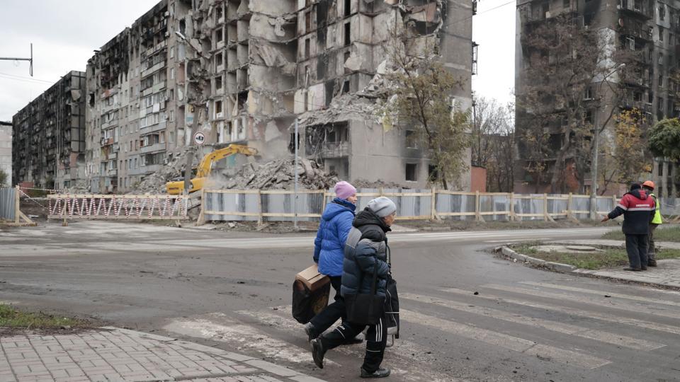 Kvinde passerer udbombede boligblokke i havnebyen Mariupol. Den ukrainske regering mener, at mindst 25.000 mennesker blev dræbt under kampene i Mariupol. Mellem 5000 og 7000 af dem døde under murbrokkerne fra deres udbombede hjem. <i>Alexei Alexandrov/Ritzau Scanpix</i>