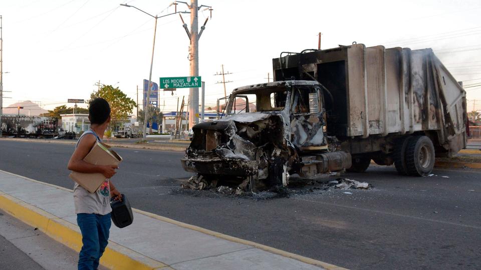 En mand passerer en udbrændt lastbil efter en politiaktion, hvor Ovidio Guzmán, søn til narkobaronen Joaquin «El Chapo» Guzmán, blevet taget til fange i delstaten Sinaloa i det nordvestlige Mexico. <i>Juan Carlos Cruz/Ritzau Scanpix</i>