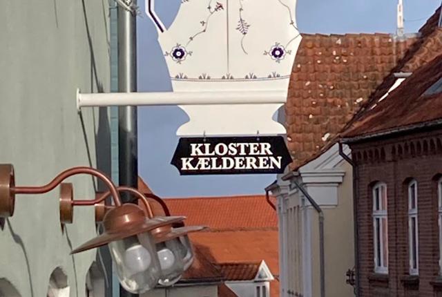 Klosterkælderen Antik & Porcelæn fylder 20 år til maj. Her ses butikkens nye skilt, inspireret af en 200 år gammel musselmalet kaffekande. 