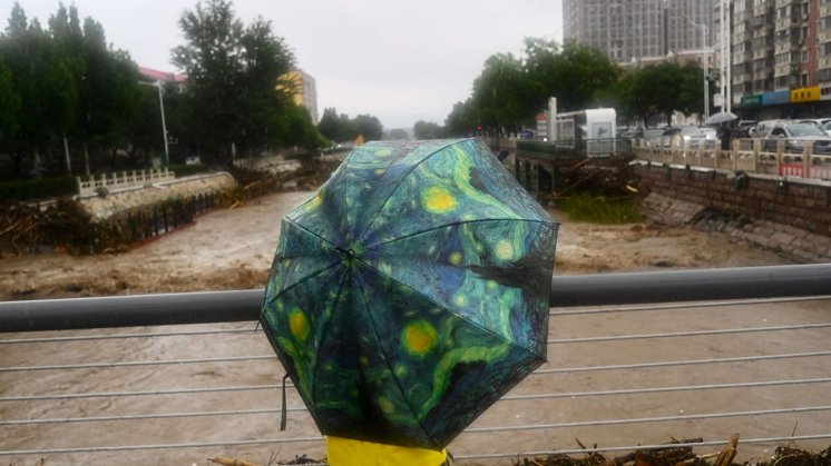 En indbygger står i regnen i Beijing mandag. Tirsdag oplyser statsmedier, at 11 personer har mistet livet på grund af den voldsomme regn i byen.