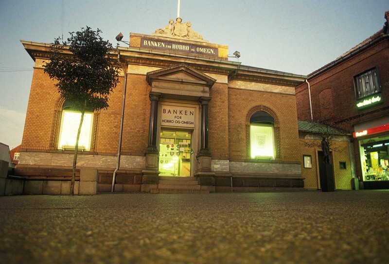 På dette arkivbillede af Himmerlandsbanken i Hobro kan man ane den allegoriske gruppe, som symboliserer handel, håndværk og landbrug. Kik på taget over indgangspartiet.