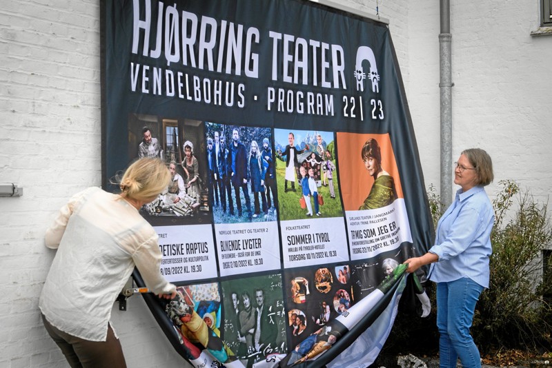 En ny teatersæson blev markeret med ophængning af det store bannere på facaden ved Vendelbohus. Leder Anette Dige Ovesen og Inger Bjørn, der er frivillige hjælper i Teaterbutikken, klarede opgaven. Foto: Creative Photo