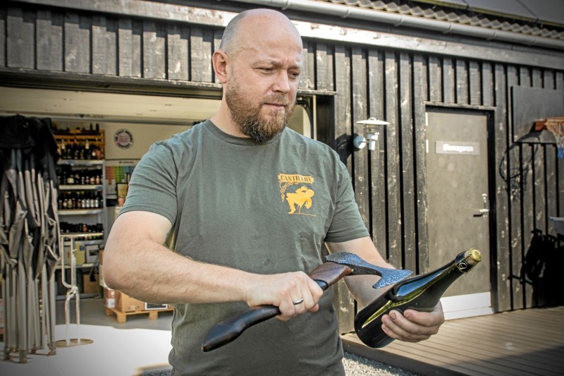 Jesper Mørkholt viser, hvordan man slår proppen af en ølflaske med en økse, når han lørdag står i spidsen for en beerwalk på Gjøl. Foto: Jesper Hansen