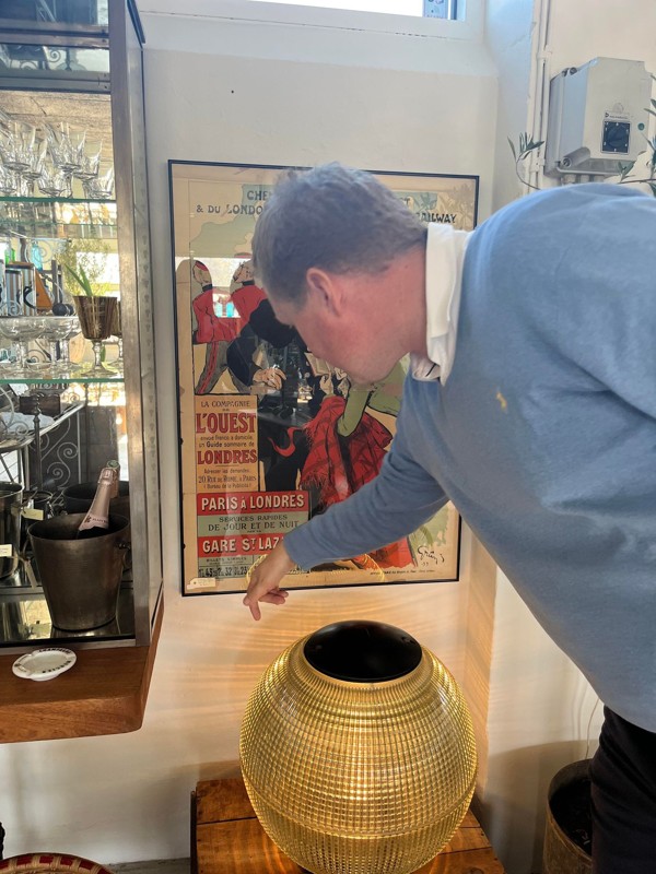Per Marc Pedersen fortæller, at plakaten her er en original fransk reklame for en ny togforbindelse – endda en af de første trykte reklamer af sin slags. Den smukke lampe er en gammel fransk gadelampe.