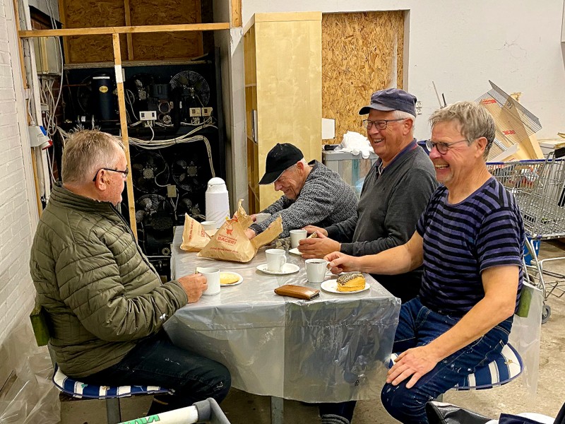 En velfortjent pause i det frivillige arbejde. Fra venstre er det Kurt Mølgaard, Ole Holmsgaard Pedersen, Poul Brander og Ove Jakobsen, som får en tår kaffe, en smurt håndværker og en onsdagssnegl fra Halvrimmen Bageri. Traktementet skyldes, at Thisted Forsikring har doneret 7.000 kroner til de frivillige, som hjælper med at istandsætte købmandsbutikken, så de kan få fyldt depoterne.