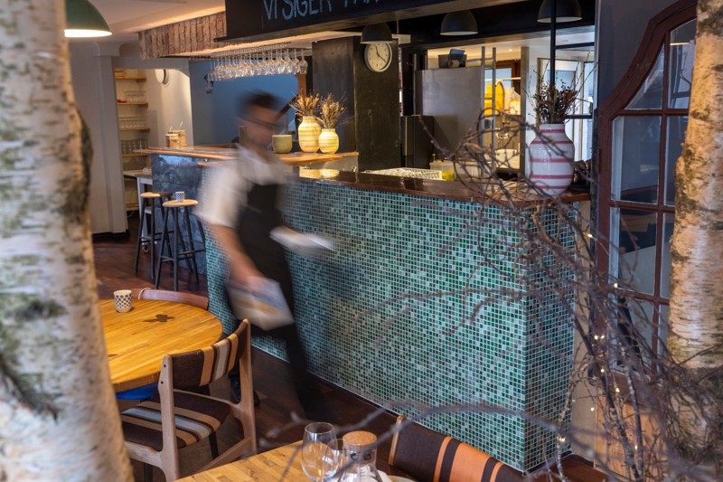 Desken midt i lokalet og farven omkring fortæller om foråret. Køkkenet er åbent og her skal Danmarks nok yngste restauratør overraske og fornøje gæsterne.